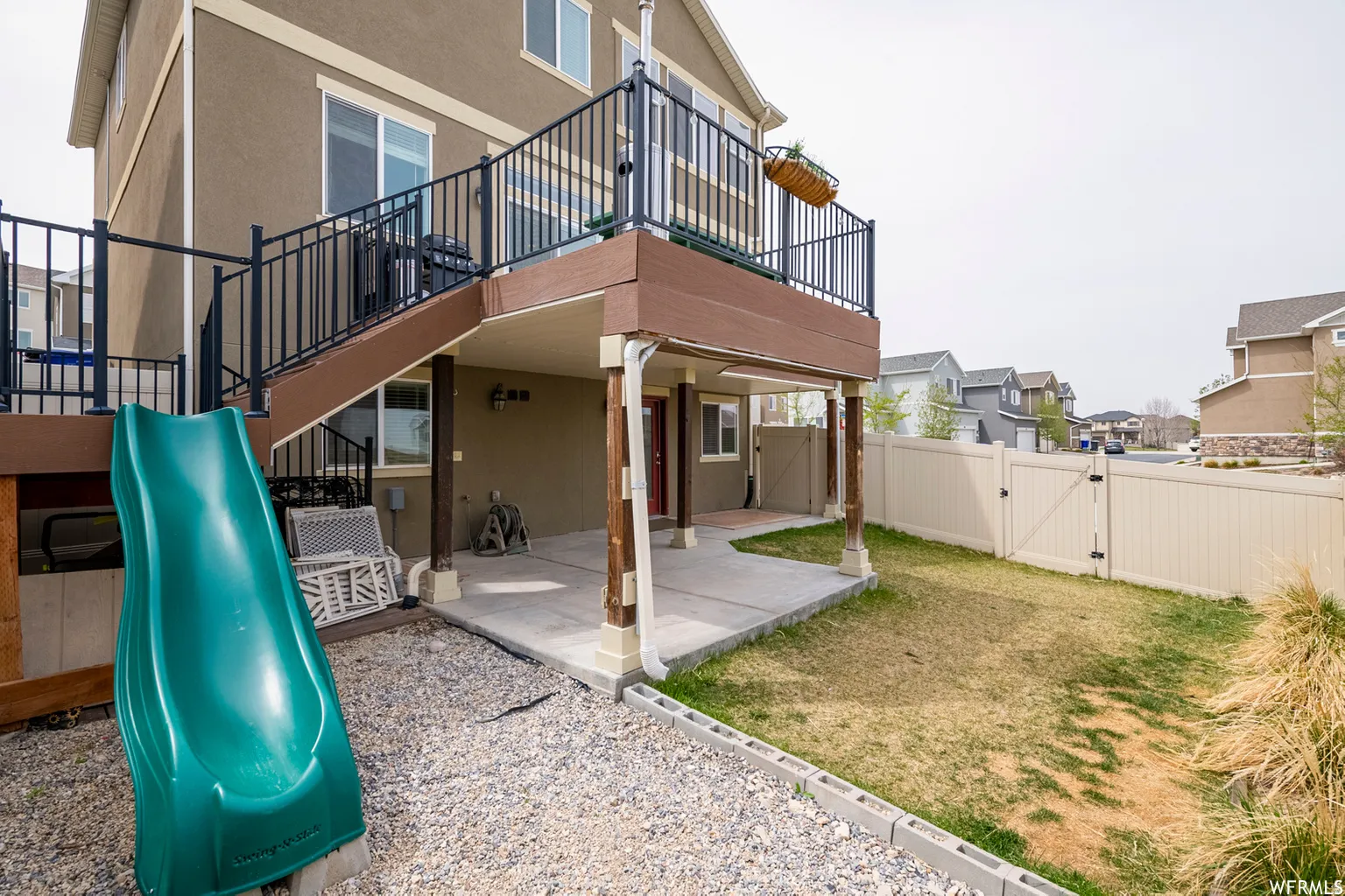Elevated deck with black metal railings, concrete patio, and fenced yard