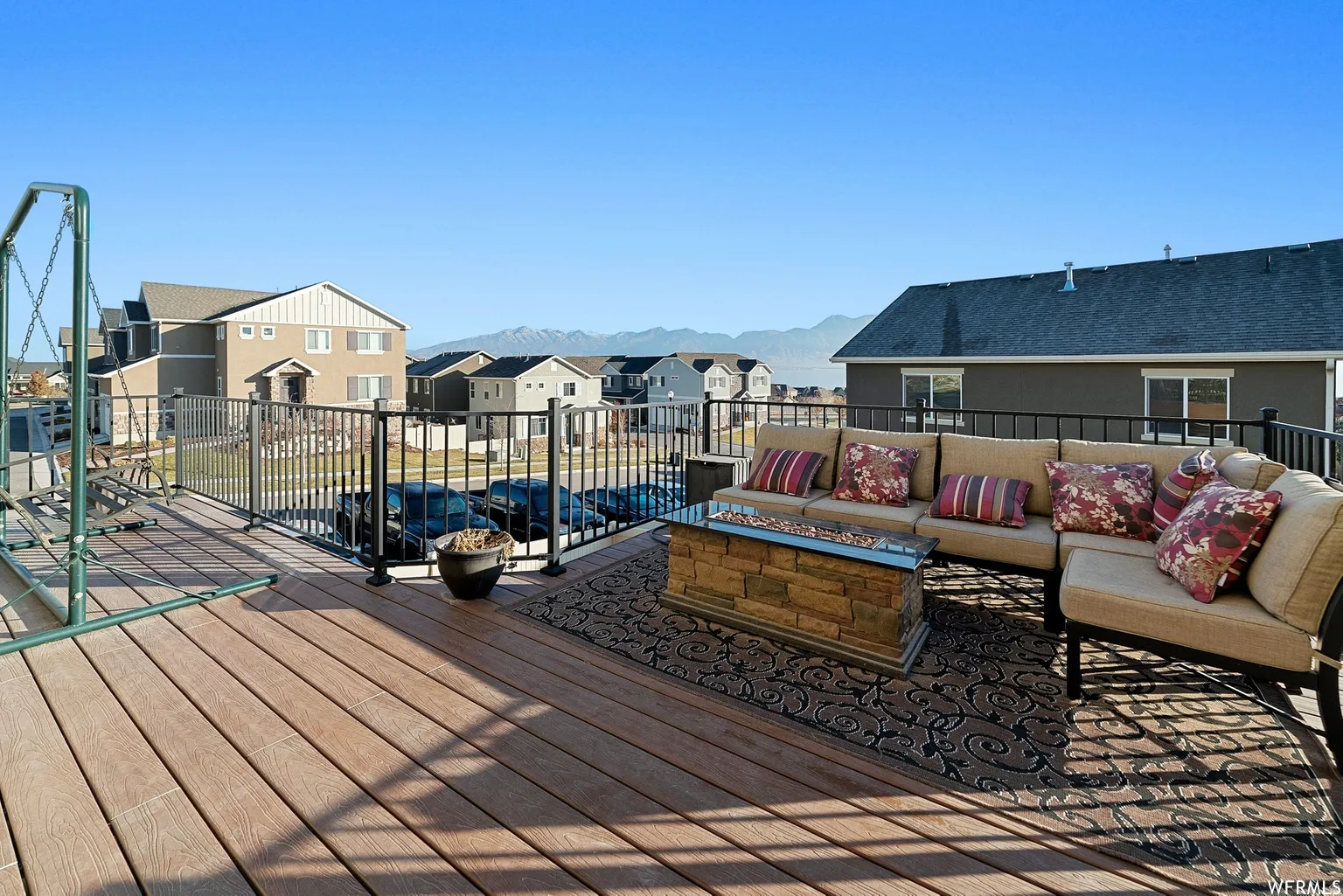 Expansive outdoor deck featuring wood-finish flooring, black metal railings, and a built-in stone fire pit