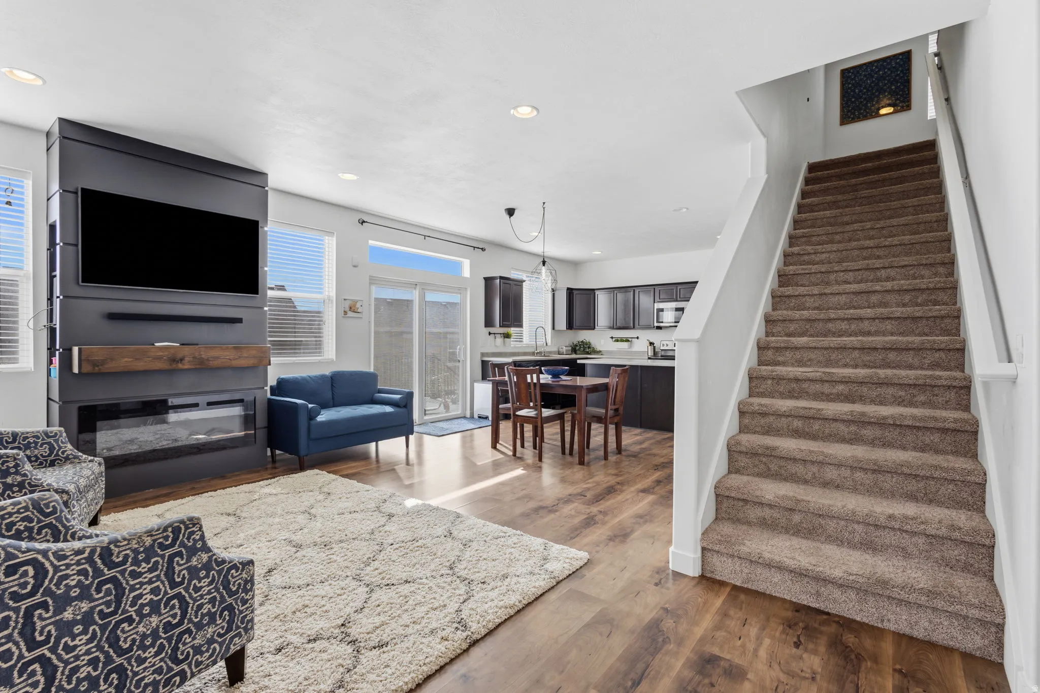 Integrated media wall with an electric fireplace, wood-finish flooring, recessed lighting, and a staircase with carpeted treads