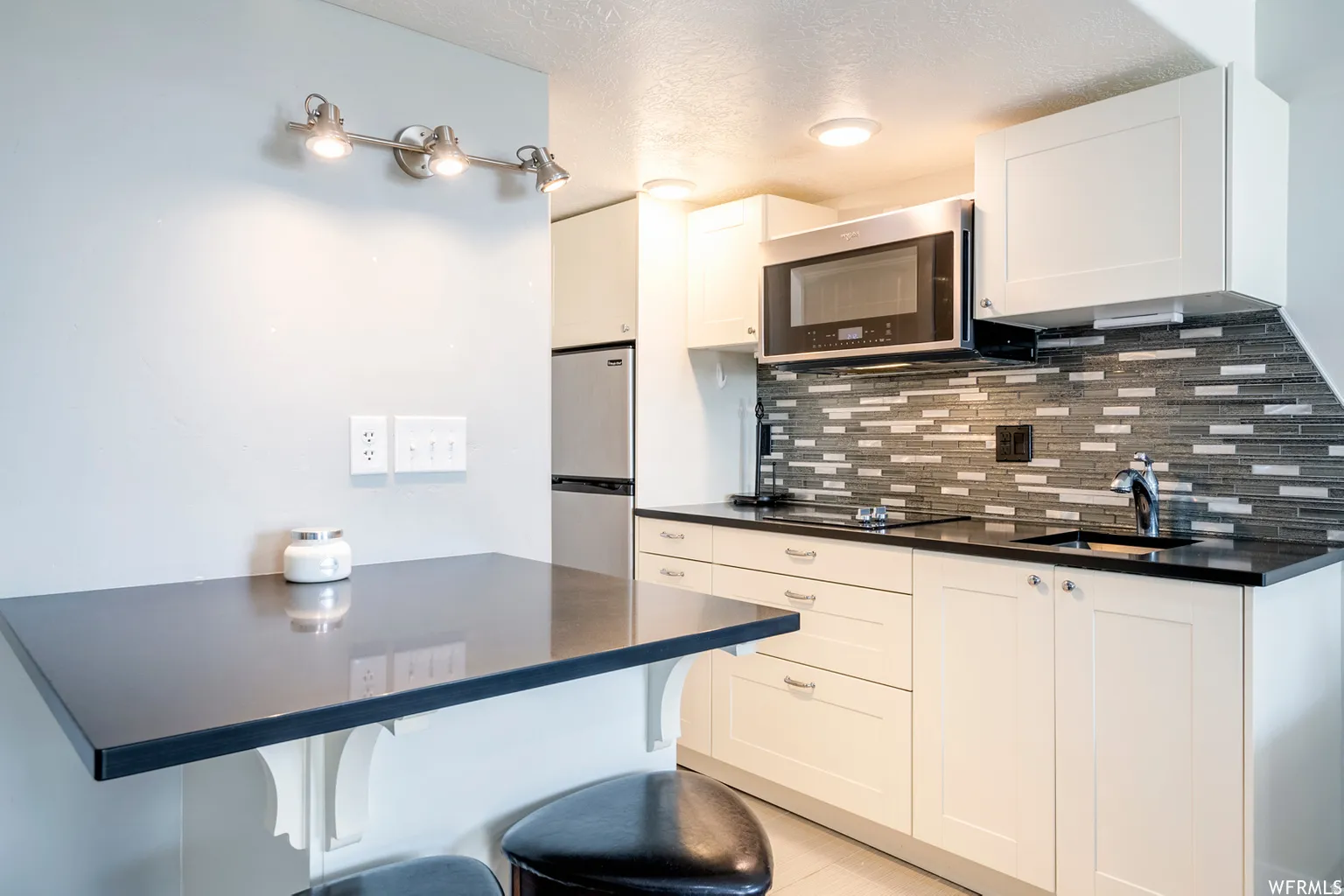 White cabinetry with dark countertops, a mosaic tile backsplash, and stainless steel appliances
