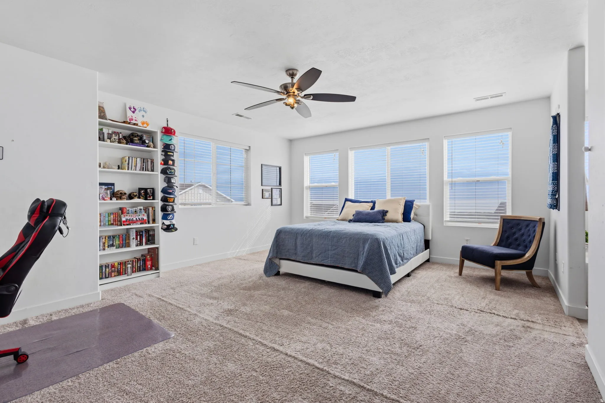 Spacious primary bedroom suite with expansive windows offering natural light and panoramic vistas, ceiling fan with brushed metal finish, wall-to-wall carpeting, built-in shelving with display space, and an adjoining seating area with hardwood-finish floo