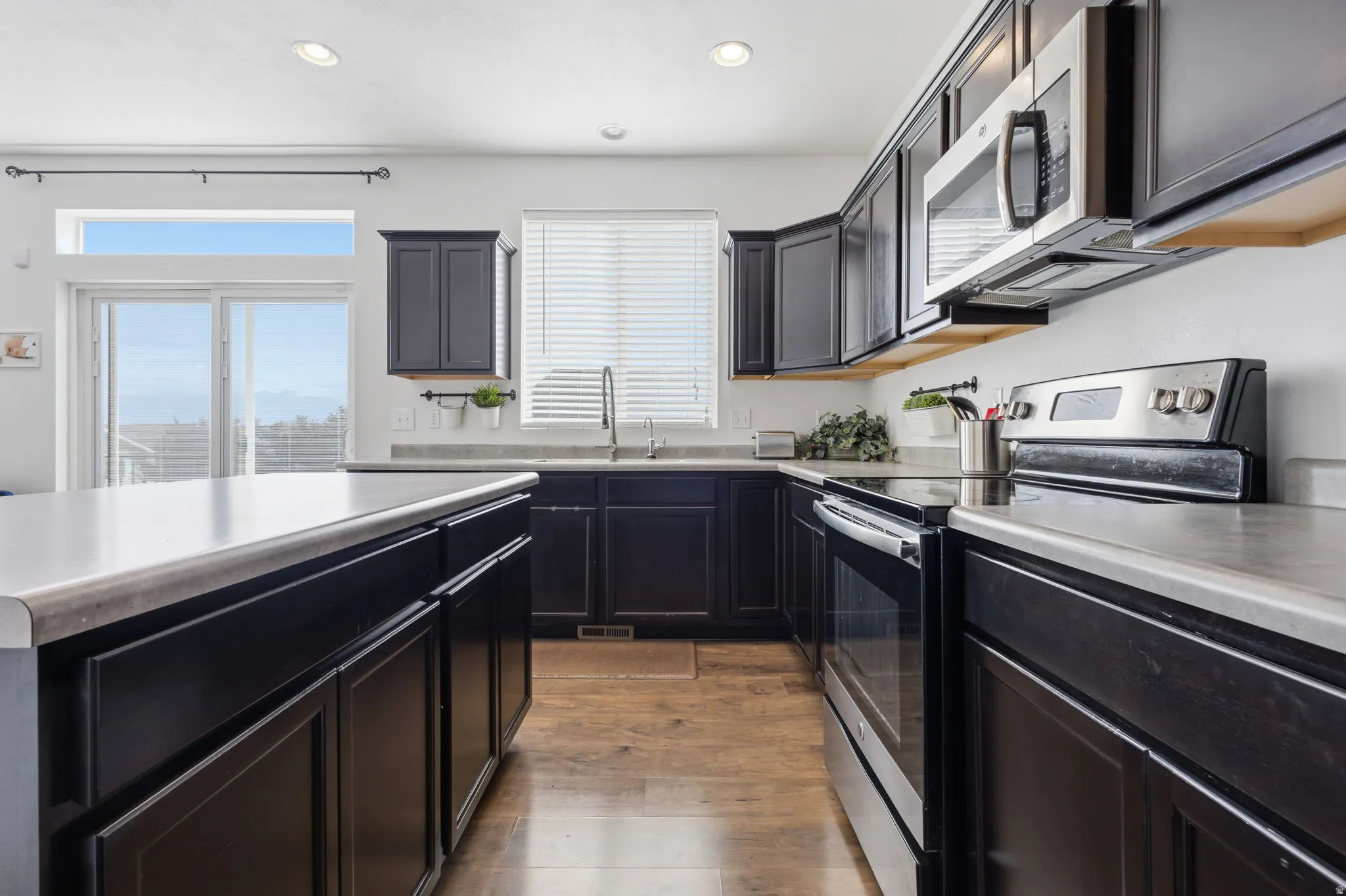 Modern kitchen featuring dark cabinetry with stainless steel appliances, white subway tile backsplash, and light-hued countertops