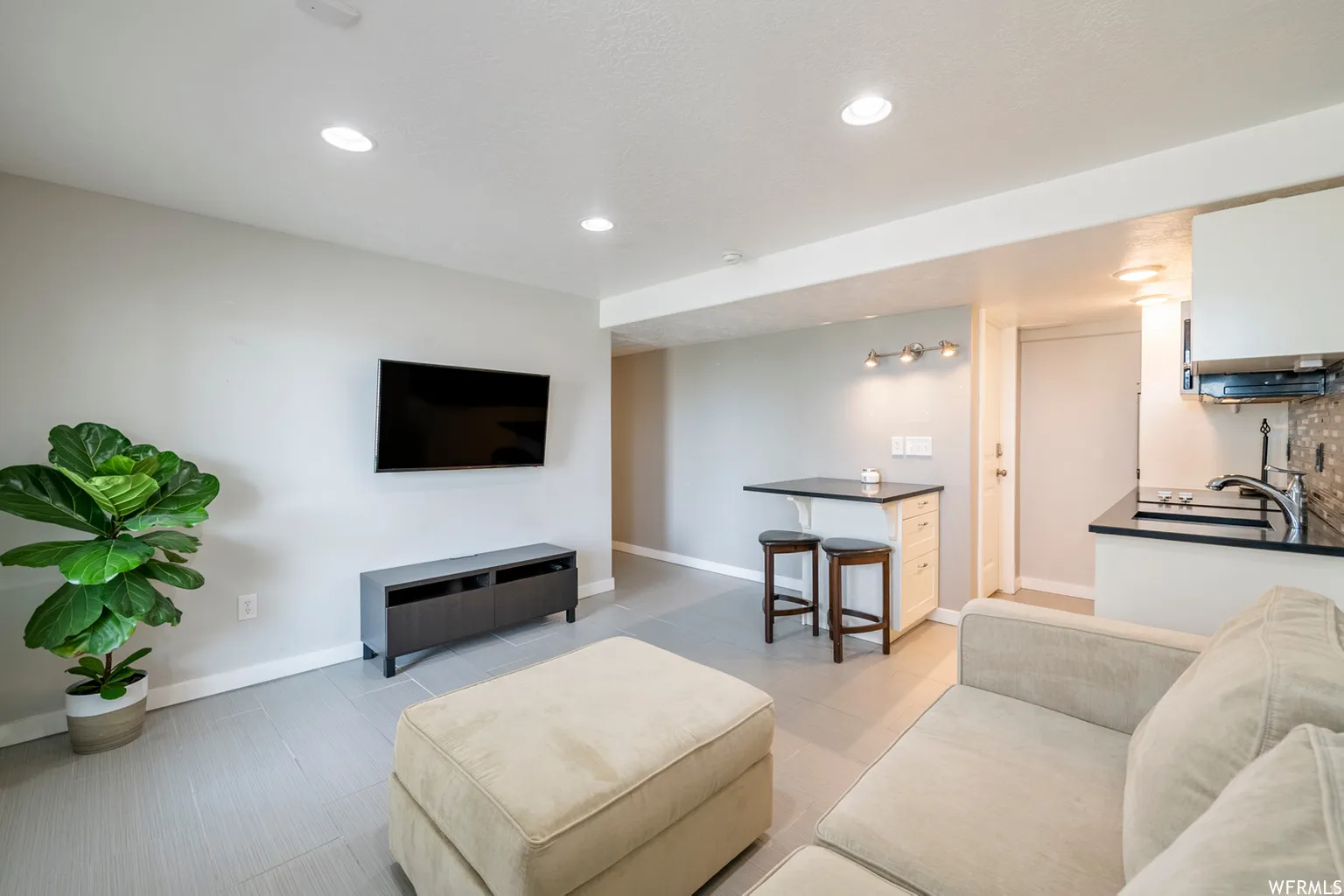 Recessed ceiling lighting, light gray walls, tile flooring, and a compact kitchen featuring a black countertop and tiled backsplash