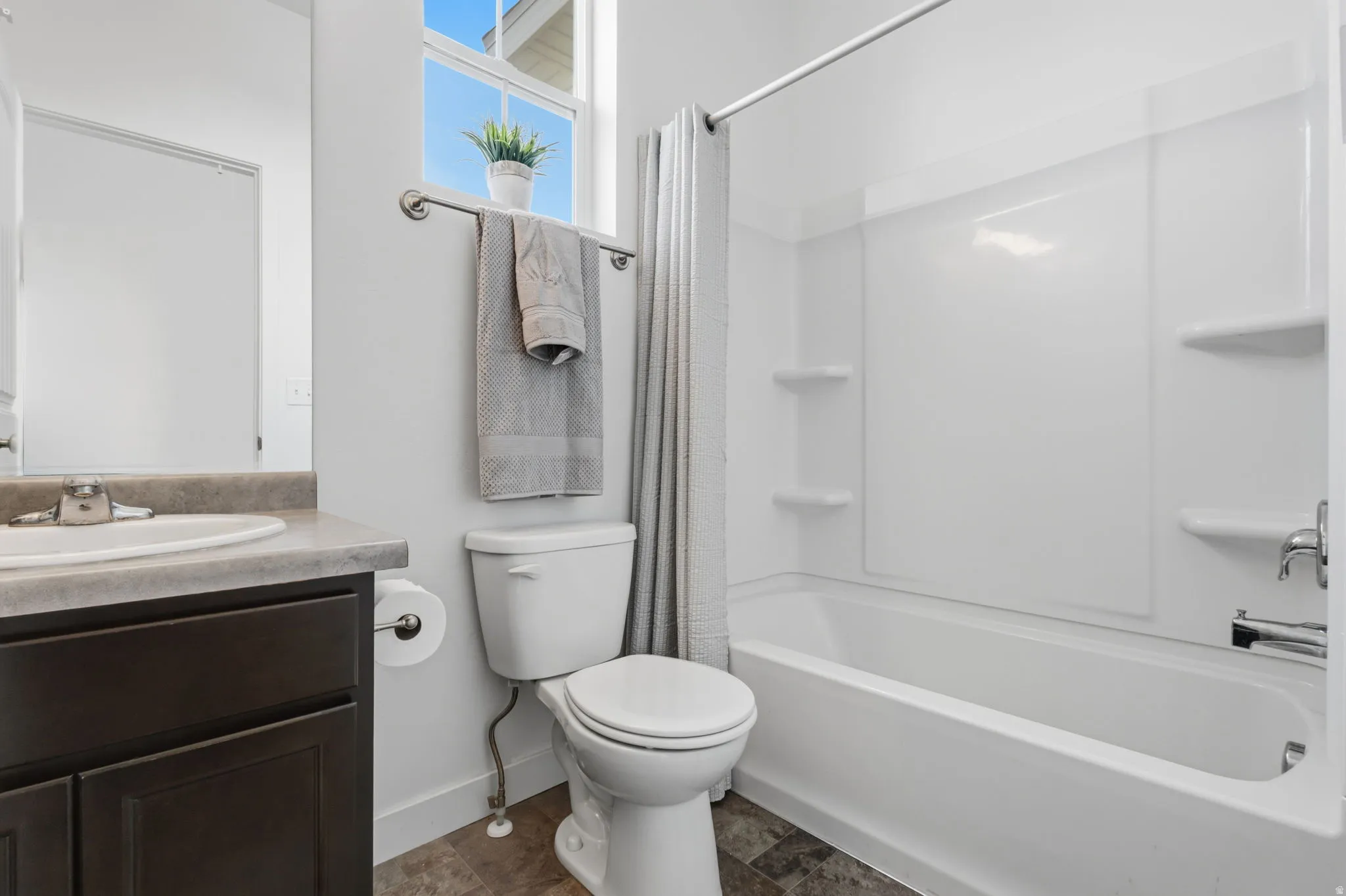 Spa-inspired bathroom featuring a dark wood vanity with integrated sink and quartz countertop, a ceramic toilet with elongated bowl, and a combined shower-tub enclosure with subway tile surround and chrome fixtures