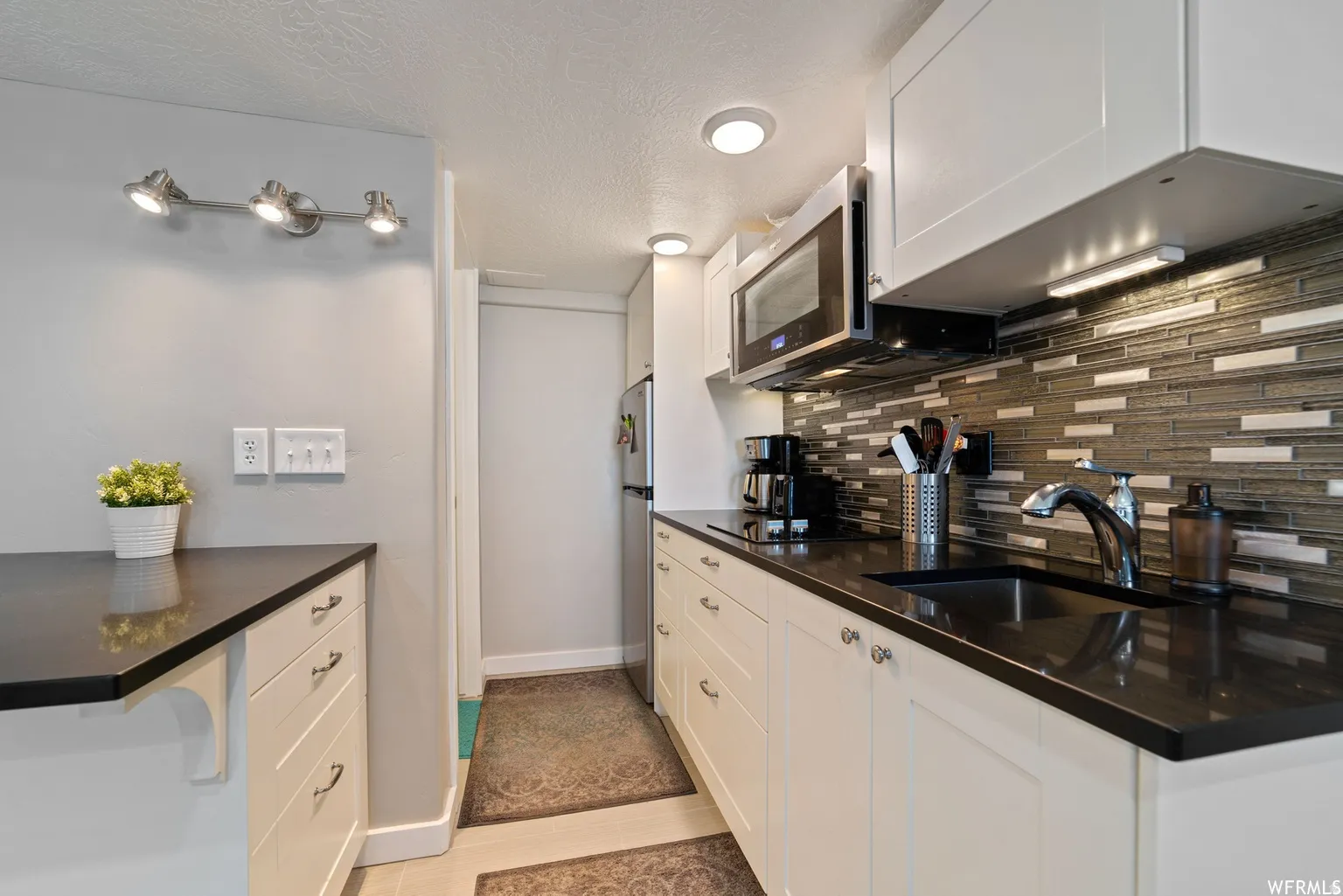 Kitchen featuring white cabinetry, dark countertops, and a mosaic tile backsplash