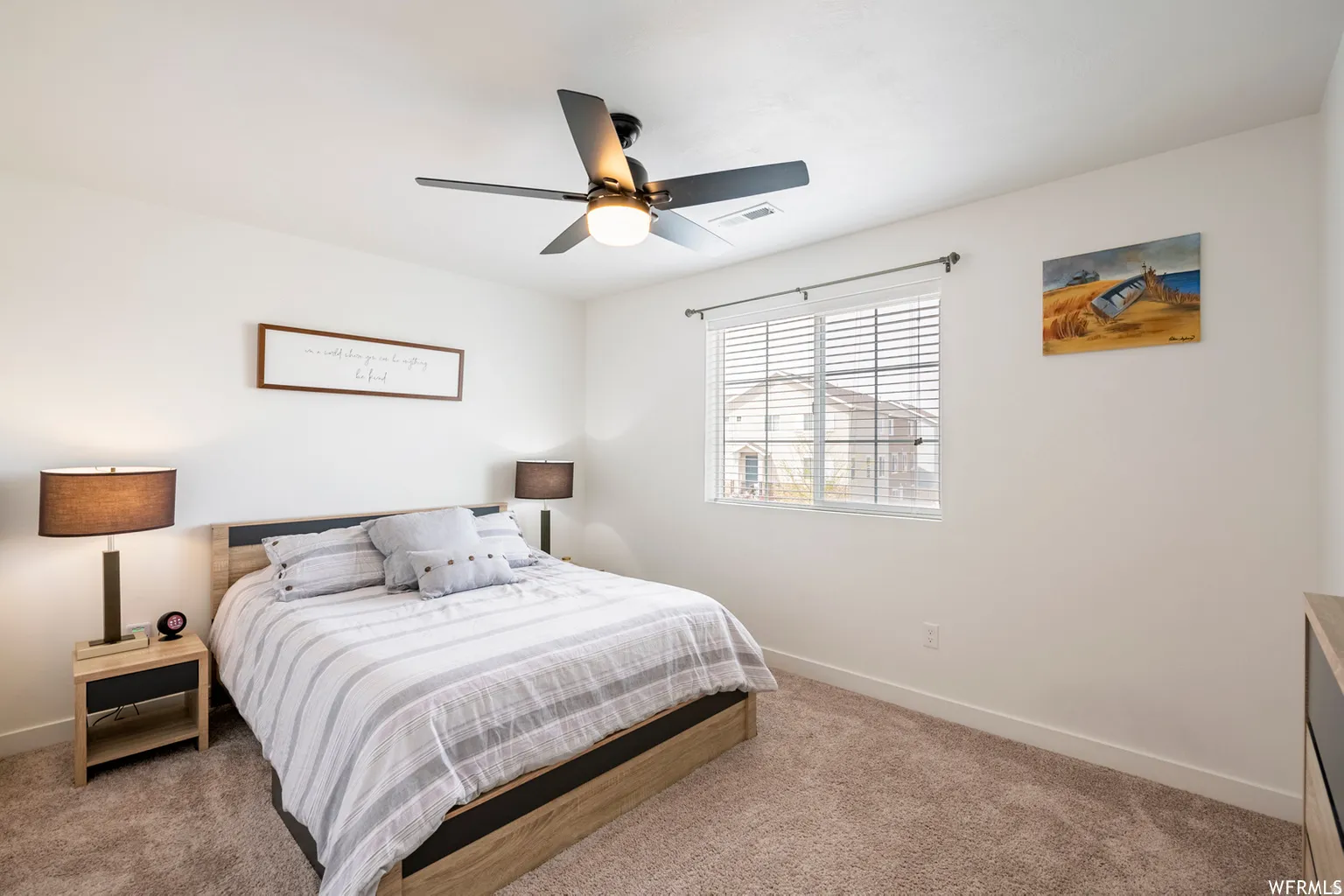 Bright secondary bedroom featuring neutral wall finishes, carpeted flooring, a ceiling fan with integrated lighting, and large shuttered window with natural light