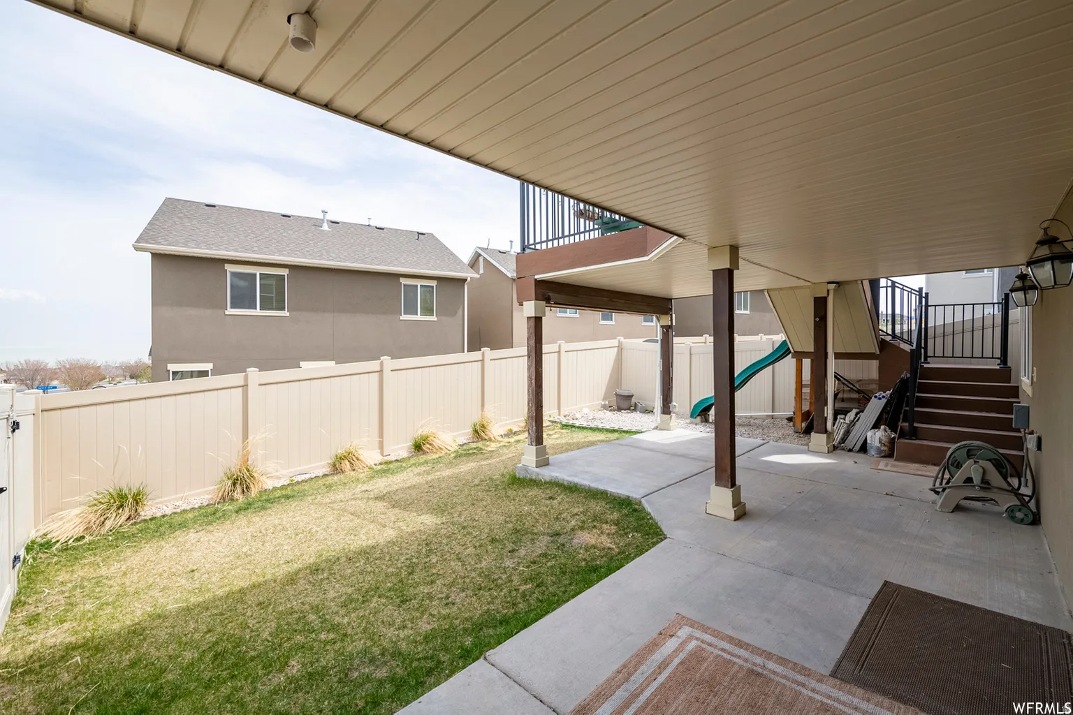 Covered patio with concrete flooring, supported by multiple posts, and enclosed by a light-toned privacy fence