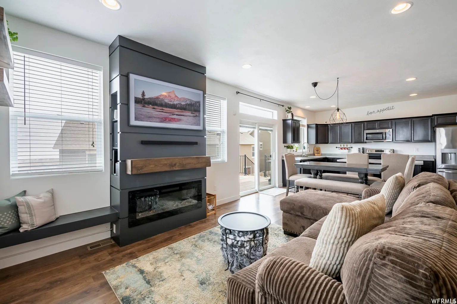 Integrated fireplace feature wall with wood mantel, built-in bench seating, wood-finish flooring, and recessed lighting