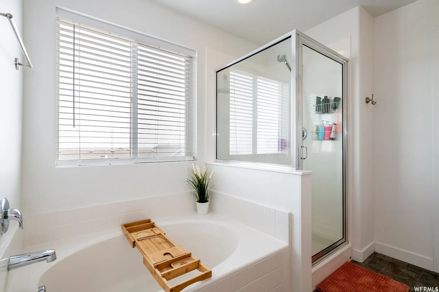 Built-in soaking tub with chrome fixtures, glass-enclosed shower, and a large window with blinds