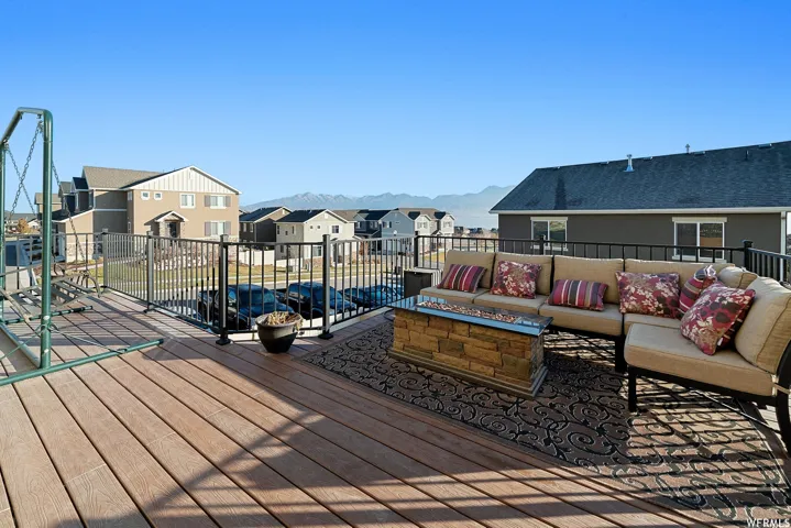 Expansive outdoor deck featuring wood-finish flooring, black metal railings, and a built-in stone fire pit