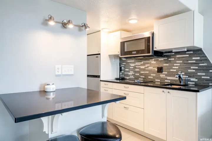 White cabinetry with dark countertops, a mosaic tile backsplash, and stainless steel appliances