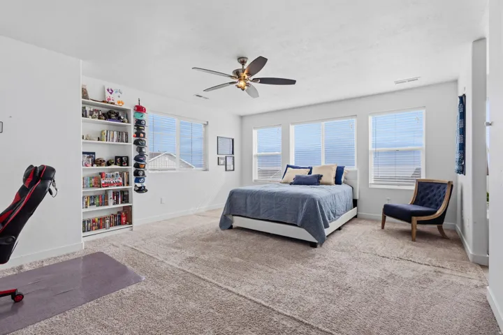 Spacious primary bedroom suite with expansive windows offering natural light and panoramic vistas, ceiling fan with brushed metal finish, wall-to-wall carpeting, built-in shelving with display space, and an adjoining seating area with hardwood-finish floo