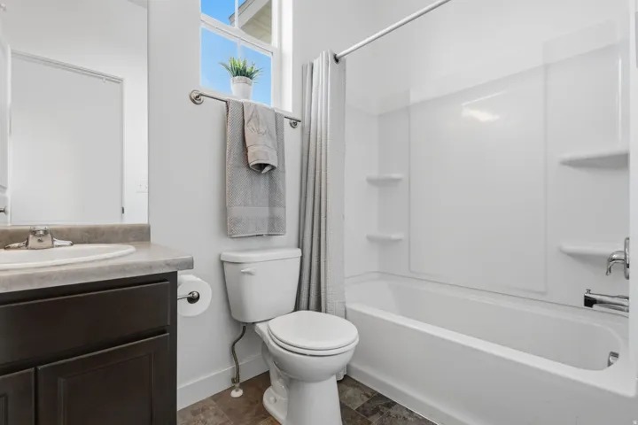 Spa-inspired bathroom featuring a dark wood vanity with integrated sink and quartz countertop, a ceramic toilet with elongated bowl, and a combined shower-tub enclosure with subway tile surround and chrome fixtures