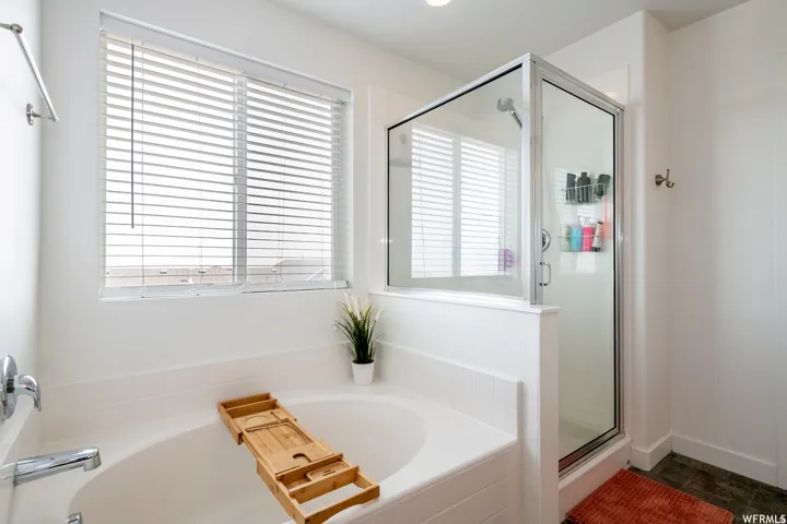 Built-in soaking tub with chrome fixtures, glass-enclosed shower, and a large window with blinds