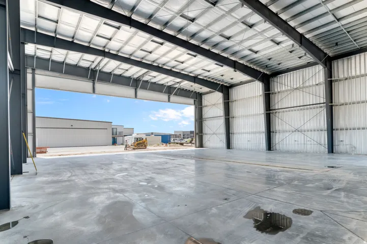 Expansive interior space featuring a polished concrete floor, exposed structural beams, insulated ceiling, and corrugated metal wall panels