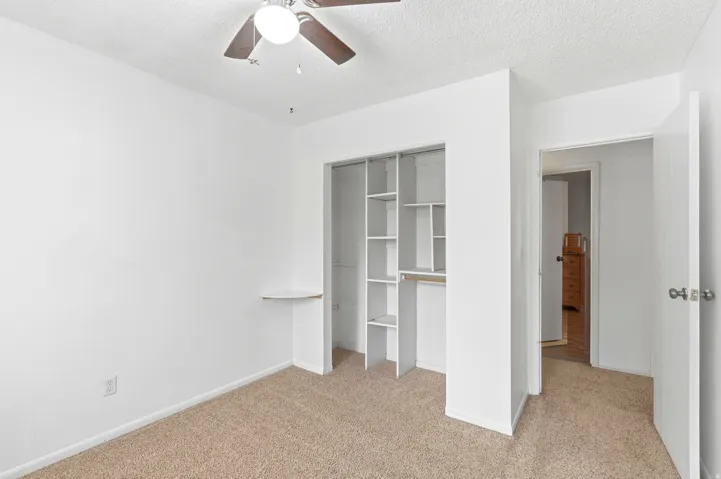 Spacious bedroom with carpeted flooring, ceiling fan, and reach-in closet featuring built-in shelving and hanging rod