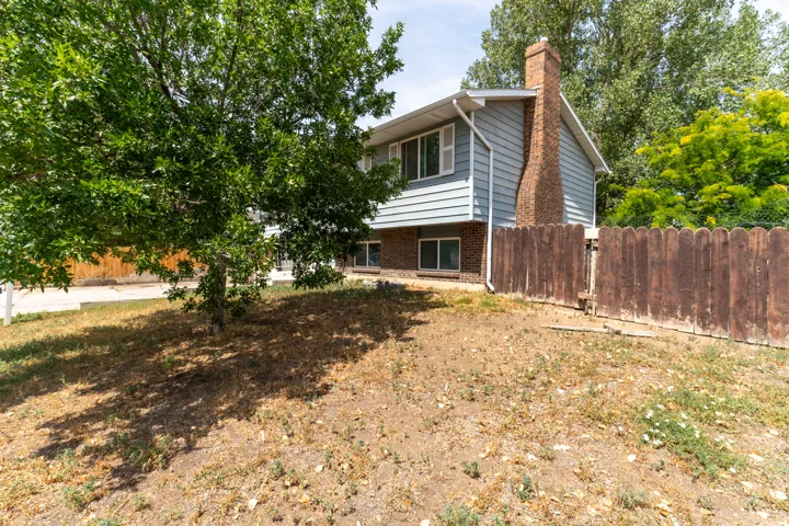 Two-story colonial with brick chimney and horizontal siding, situated on a spacious lot with mature shade trees and wooden perimeter fencing