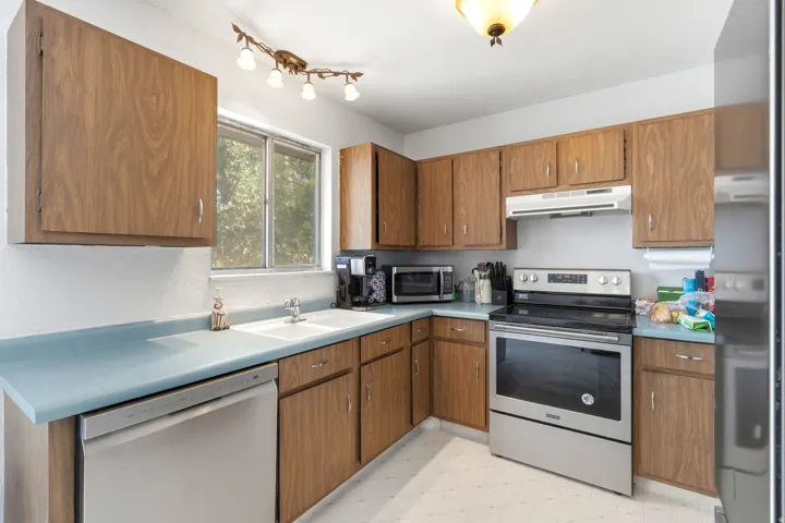 Kitchen featuring wood-finish cabinetry, light blue countertops, a double basin sink, and stainless steel appliances