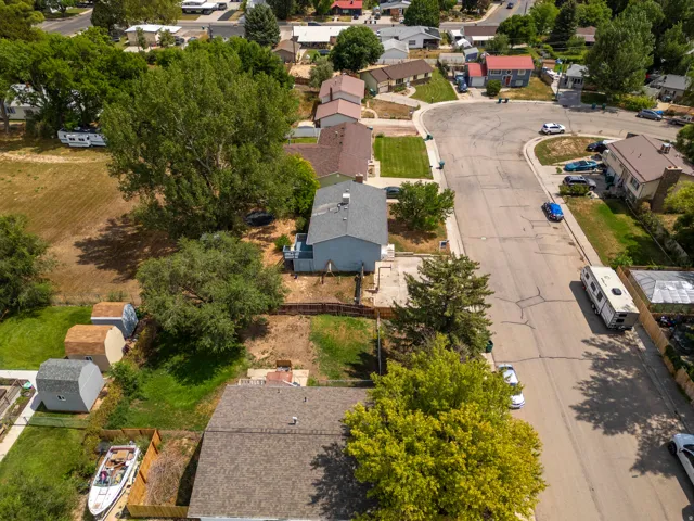Aerial view showcasing a residence with an updated roof, manicured lawn, mature landscaping, and a tree-lined lot situated in an established neighborhood with nearby residential properties