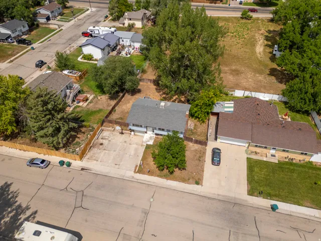 Aerial view showcasing a single-story residence on a generously sized lot with mature trees, concrete driveway, and established landscaping