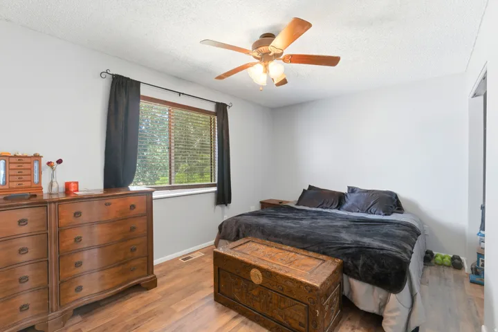 Wood-finish flooring, ceiling fan with integrated lighting, window with blinds, and light gray wall paint