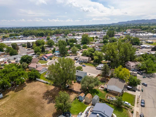 Aerial view showcasing a residential property situated on a generous lot with mature landscaping, including established trees and manicured lawn areas
