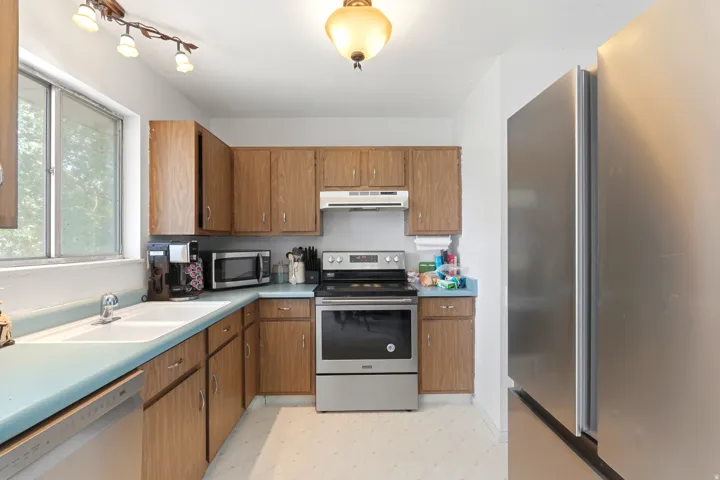 Wood-finish cabinetry, light blue countertops, a double basin sink, and stainless-steel appliances including a refrigerator and range