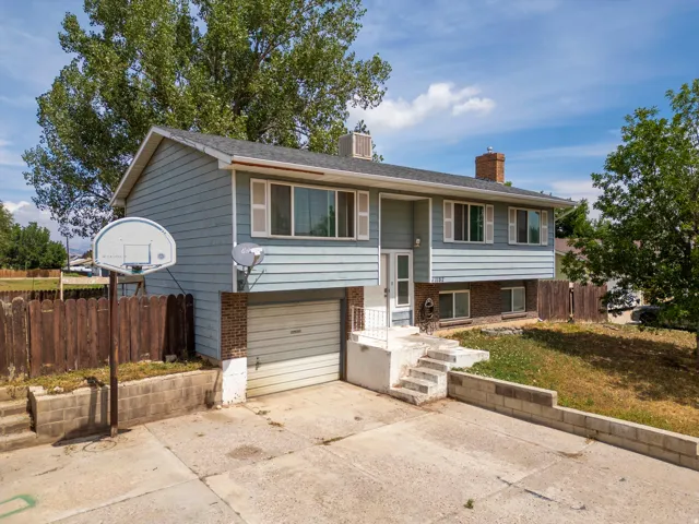 Split-level home featuring a freshly paved driveway, attached two-car garage with paneled door, composite siding exterior, and mature landscaping with established trees