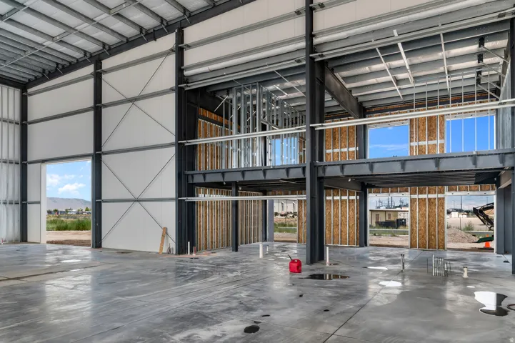 Expansive interior with exposed structural steel beams, concrete flooring, upper-level framed sections, and multiple large openings