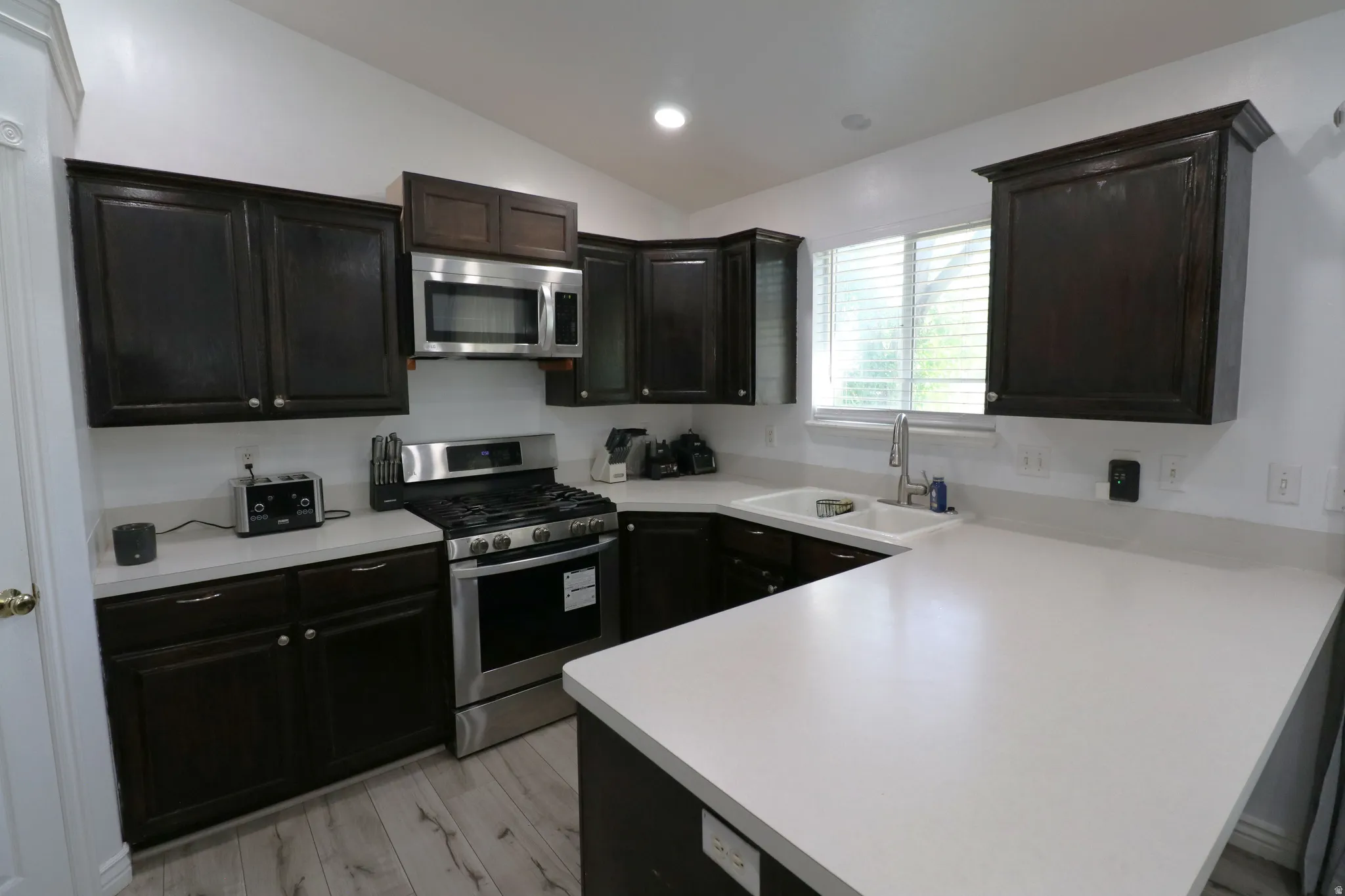 Kitchen featuring dark wood cabinetry, light countertops, stainless steel appliances, and wood-finish flooring