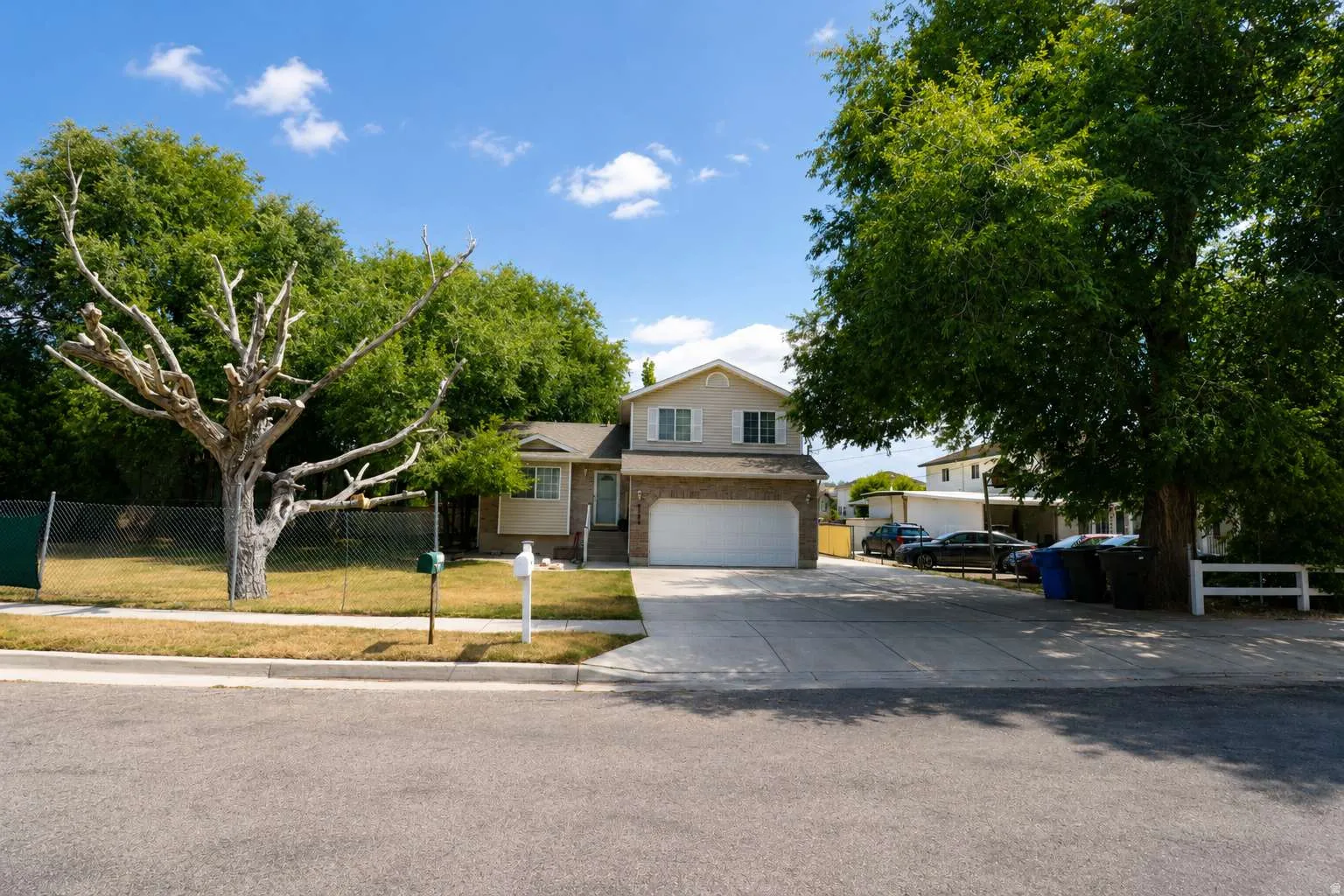Two-story residence featuring a two-car garage, concrete driveway, and an expansive front yard with mature trees