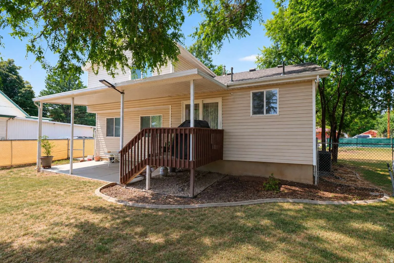 Expansive backyard featuring a covered patio, wood deck, and chain-link fencing