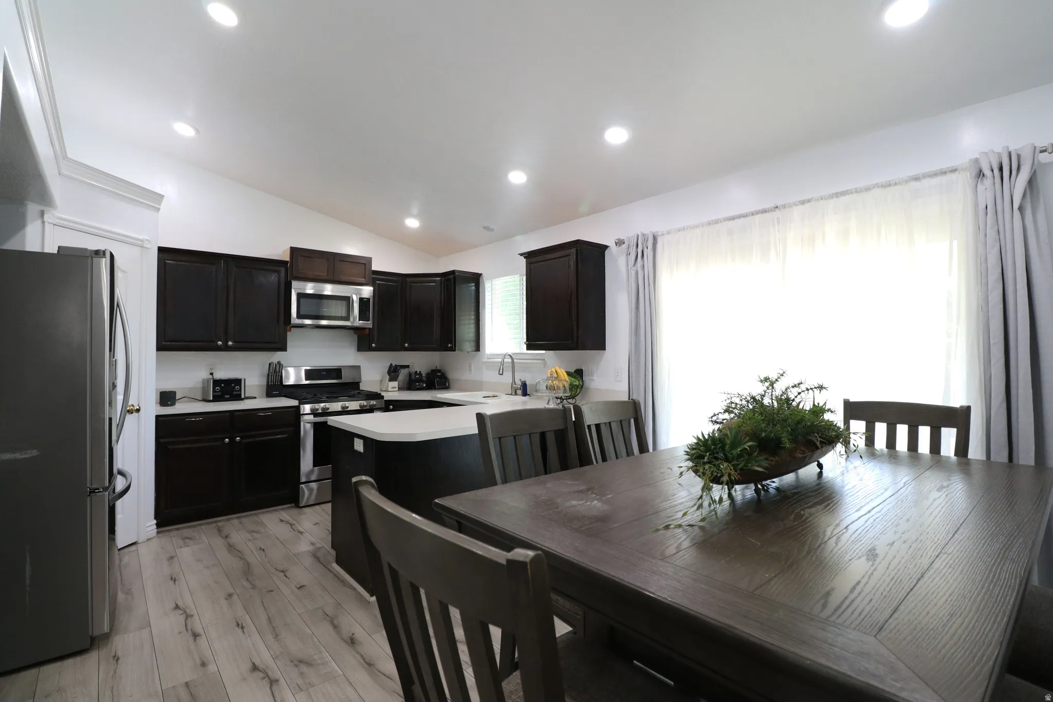 Kitchen featuring dark wood cabinetry, stainless steel appliances, light-toned countertops, and wood-finish flooring