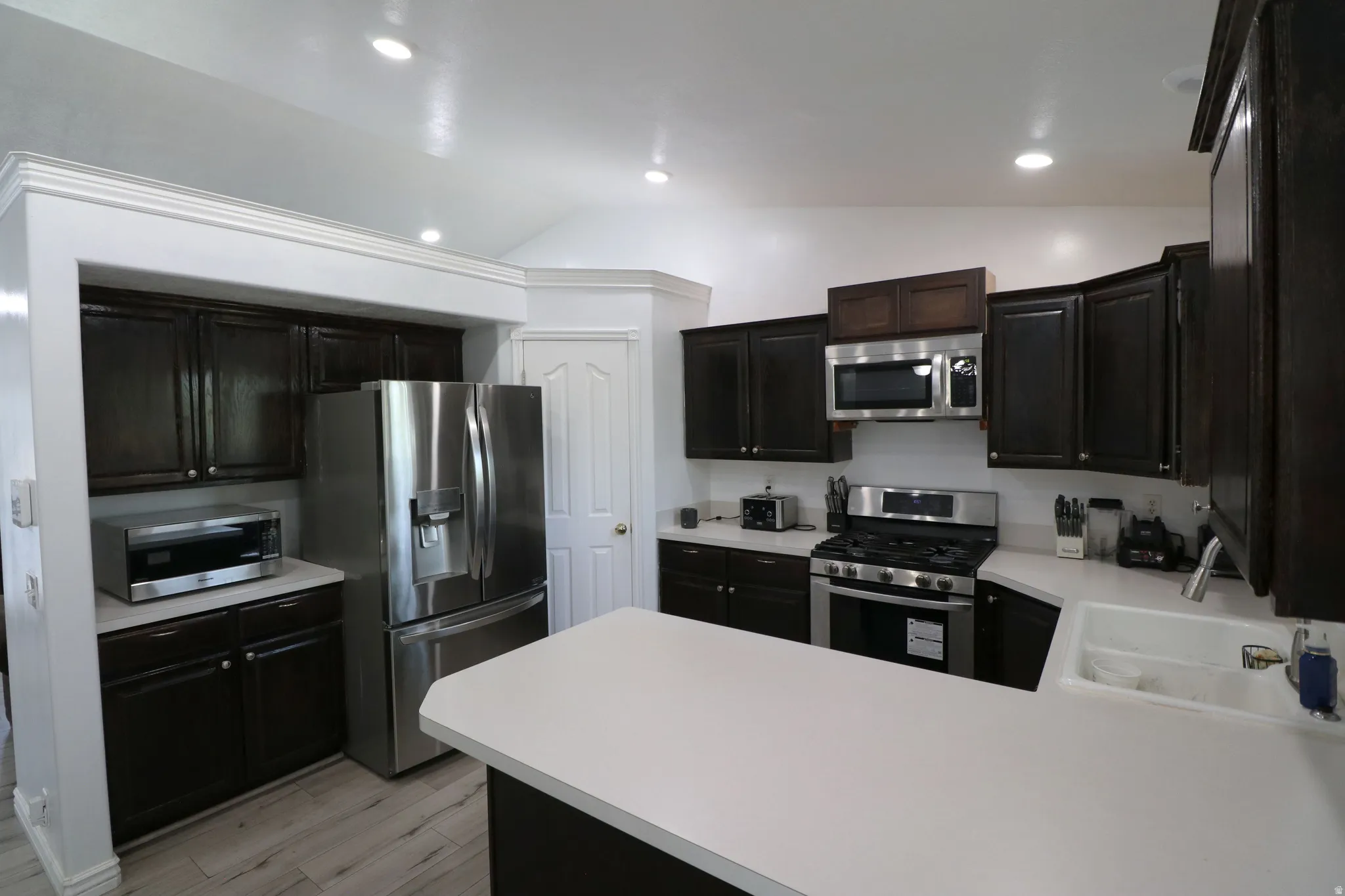 Kitchen featuring dark wood cabinetry, light countertops, stainless steel appliances, and recessed lighting