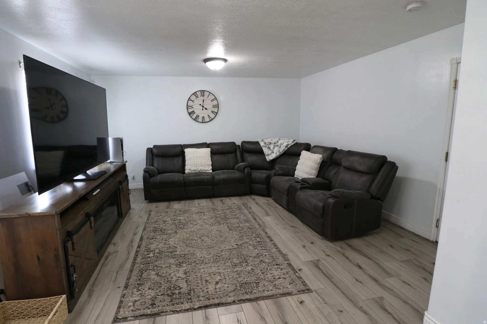 Spacious living area featuring a sectional layout with ample seating, wood-finish flooring throughout, neutral wall finishes, and a wall-mounted flat-screen television