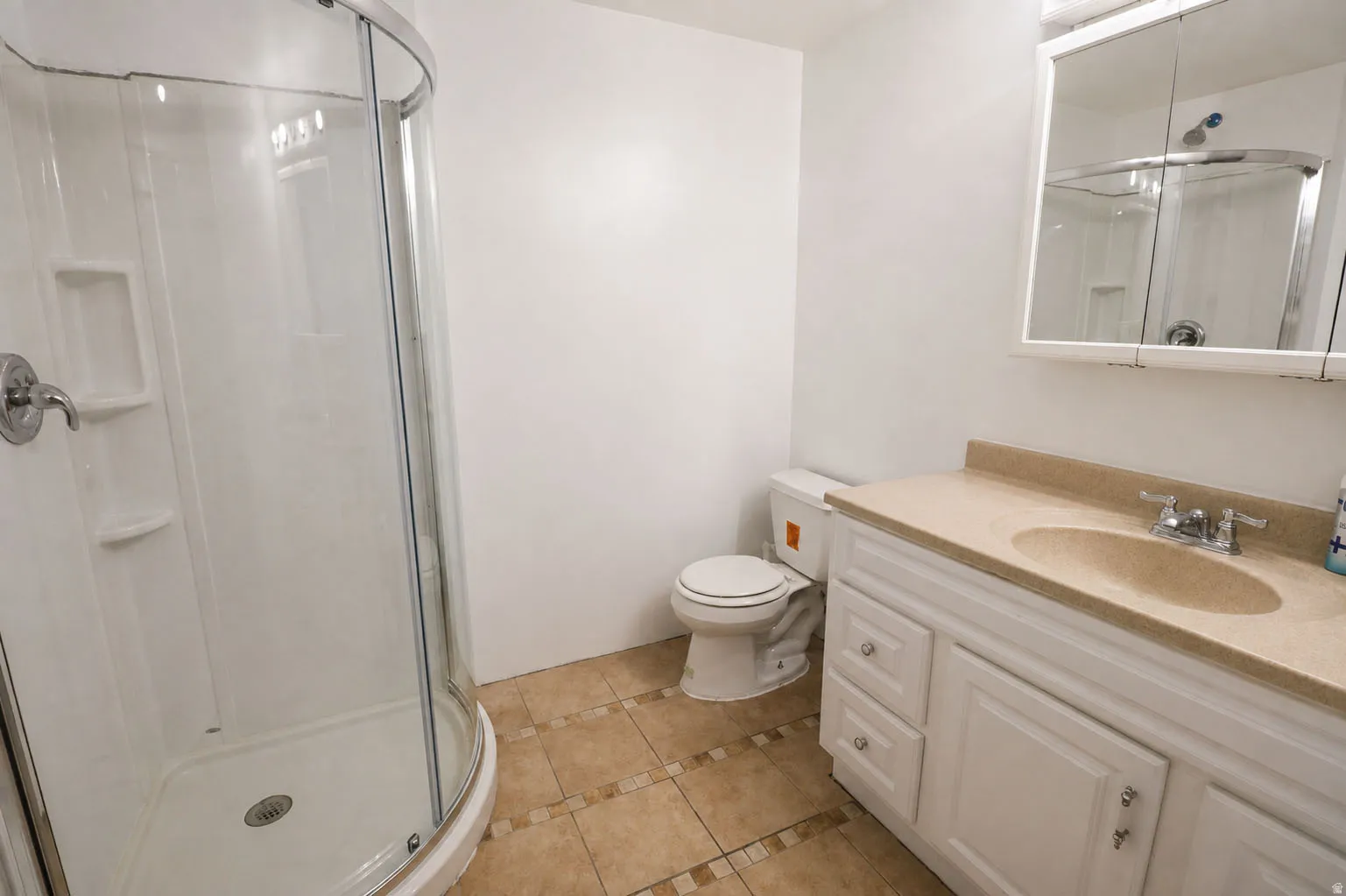 Curved glass shower enclosure, white shower surround with integrated shelving, vanity with integrated sink and chrome fixtures, white vanity cabinetry with drawer storage, and square floor tiles