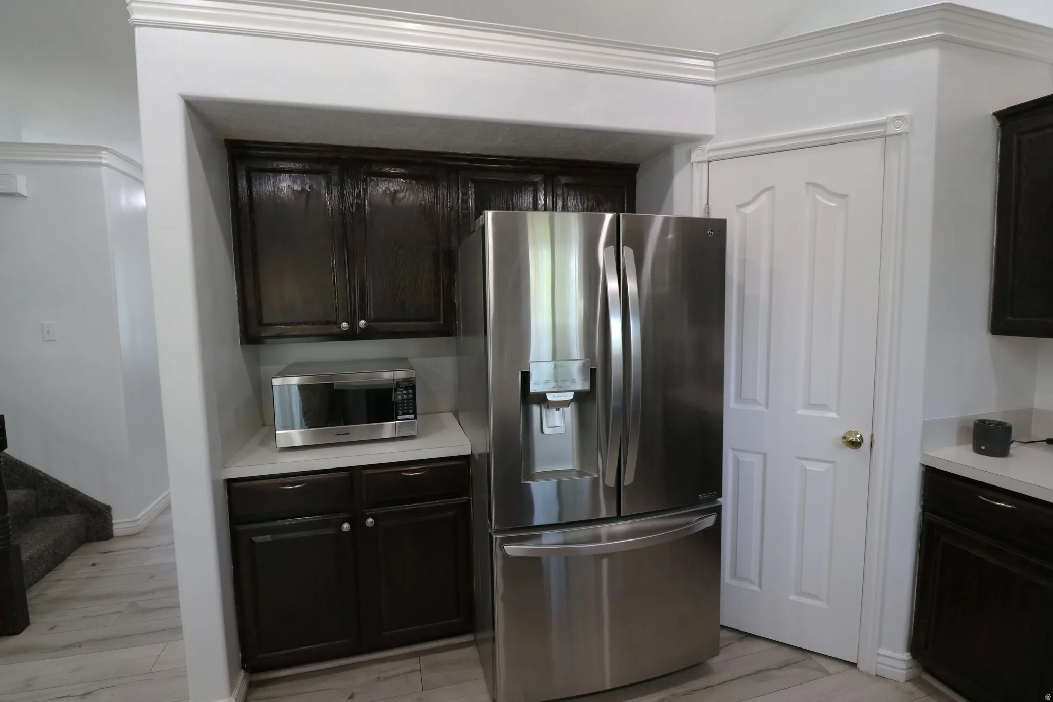 Stainless steel refrigerator, dark wood-finish cabinetry, light-toned countertop, and crown molding