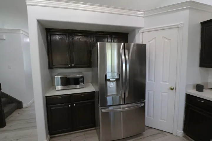 Stainless steel refrigerator, dark wood-finish cabinetry, light-toned countertop, and crown molding