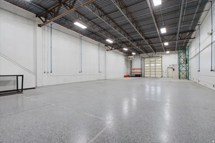 High ceilings with exposed metal trusses, polished concrete flooring, a large roll-up door, and white painted walls