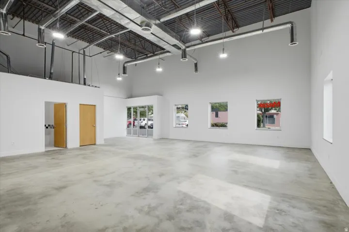 Expansive open-concept space featuring polished concrete flooring, exposed ceiling with ductwork, multiple windows, and a glass-paneled entry