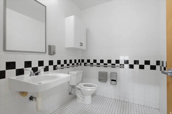 White ceramic wall-mounted sink with chrome faucet, large framed mirror, built-in wall cabinet, and white square floor tiles
