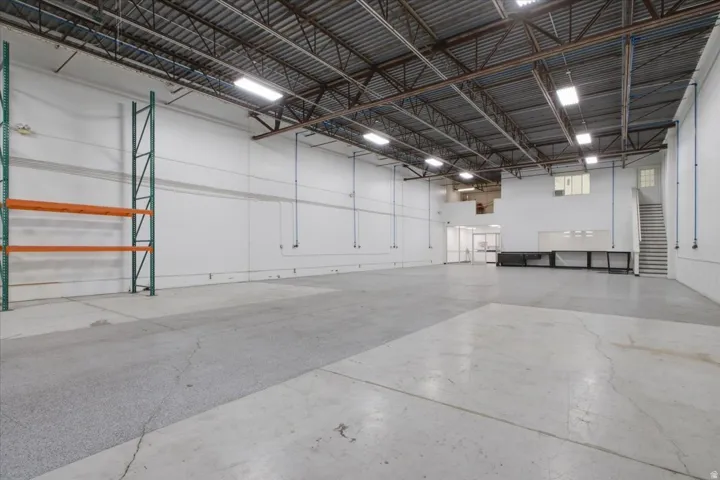 High ceilings with exposed structural beams, polished concrete flooring, integrated lighting, built-in shelving, and a two-story layout with staircase access