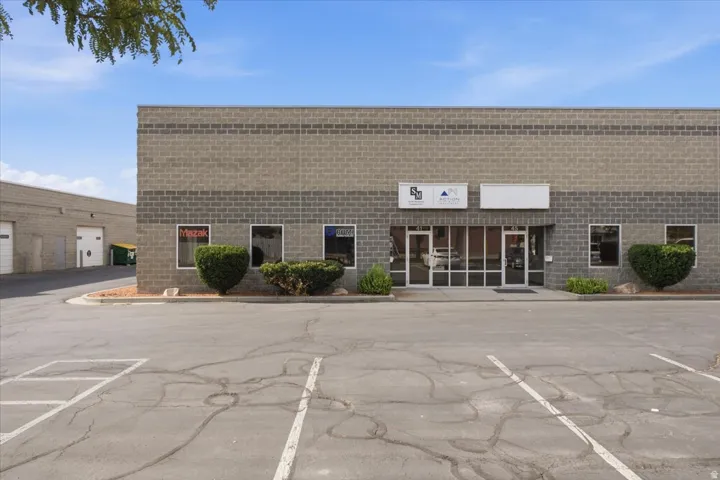 Brick exterior with multiple windows, glass entry doors, and a paved parking area