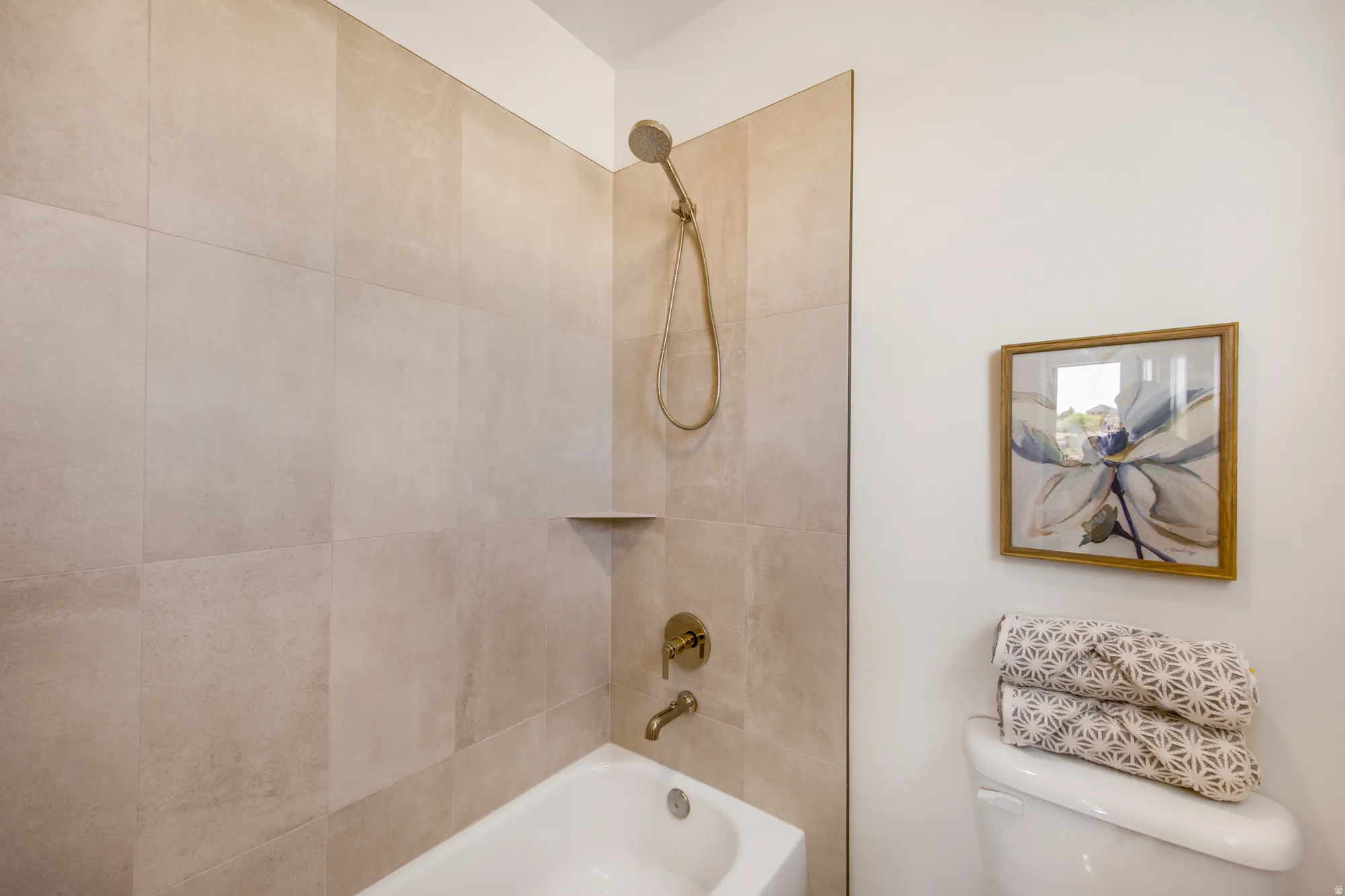Bathtub with light-colored tile surround, integrated shower niche, and brushed brass fixtures