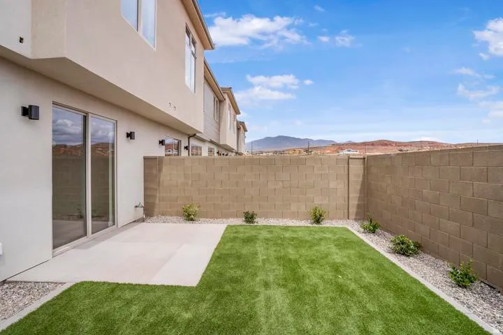 Private patio area featuring a concrete pad, artificial turf, and decorative gravel with plantings