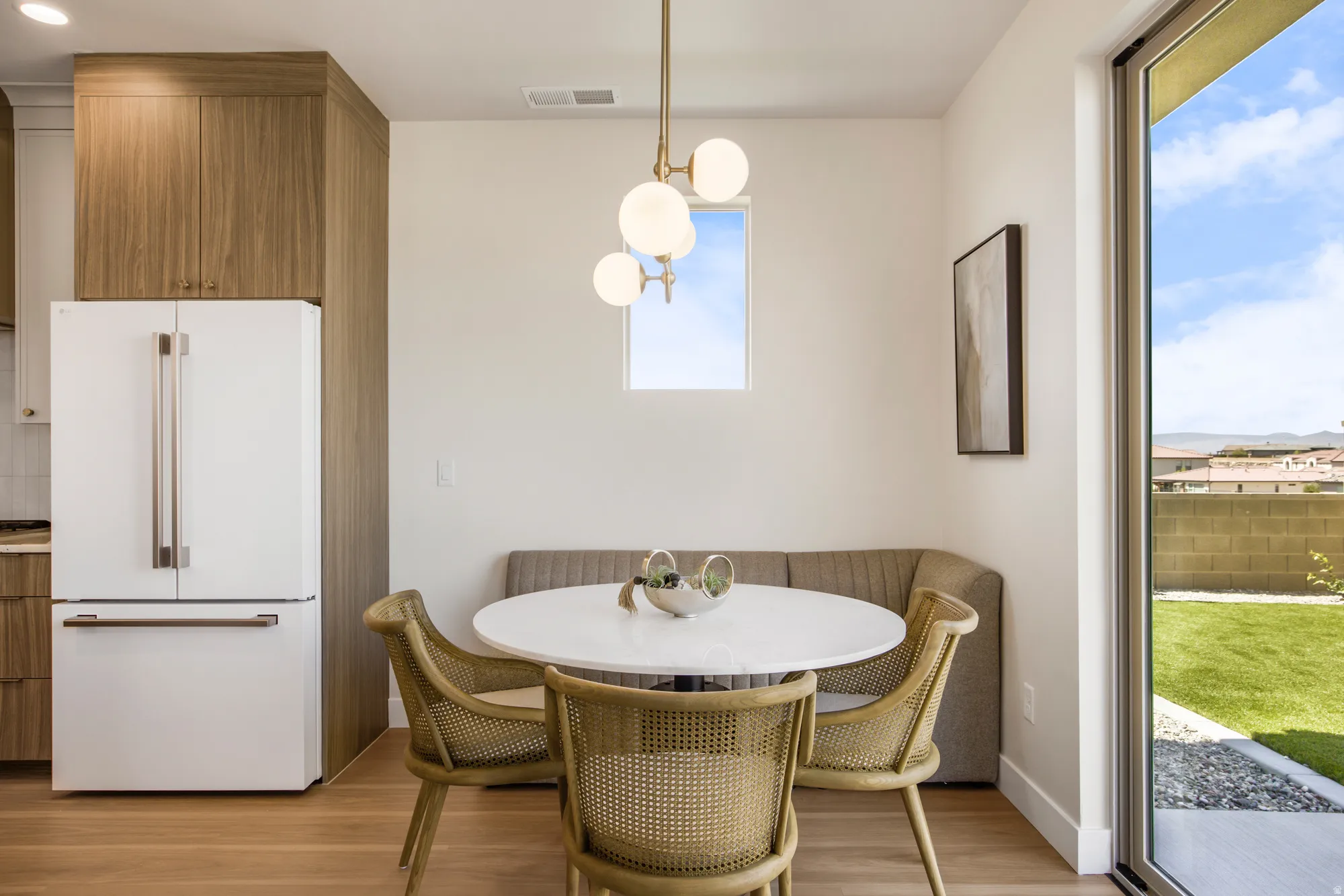 Wood-finish flooring, built-in kitchen cabinetry, white refrigerator, large glass sliding door, and a manicured lawn