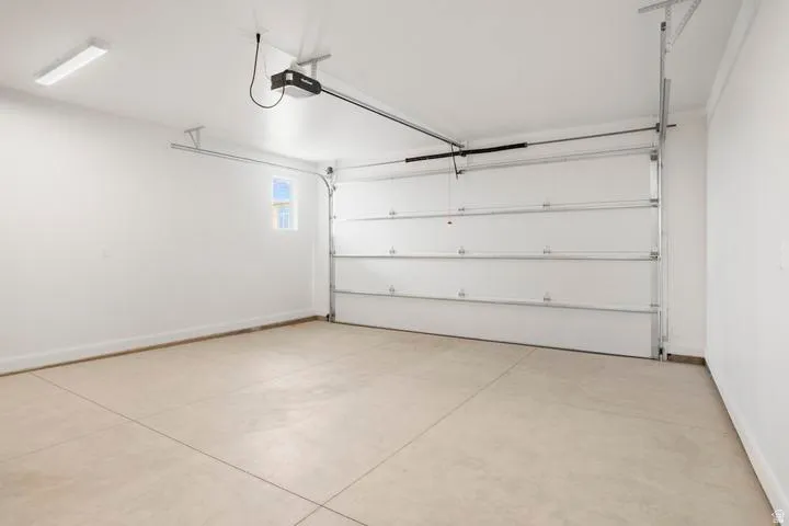 Spacious garage featuring a sectional overhead door, automatic opener, concrete flooring, and a single window