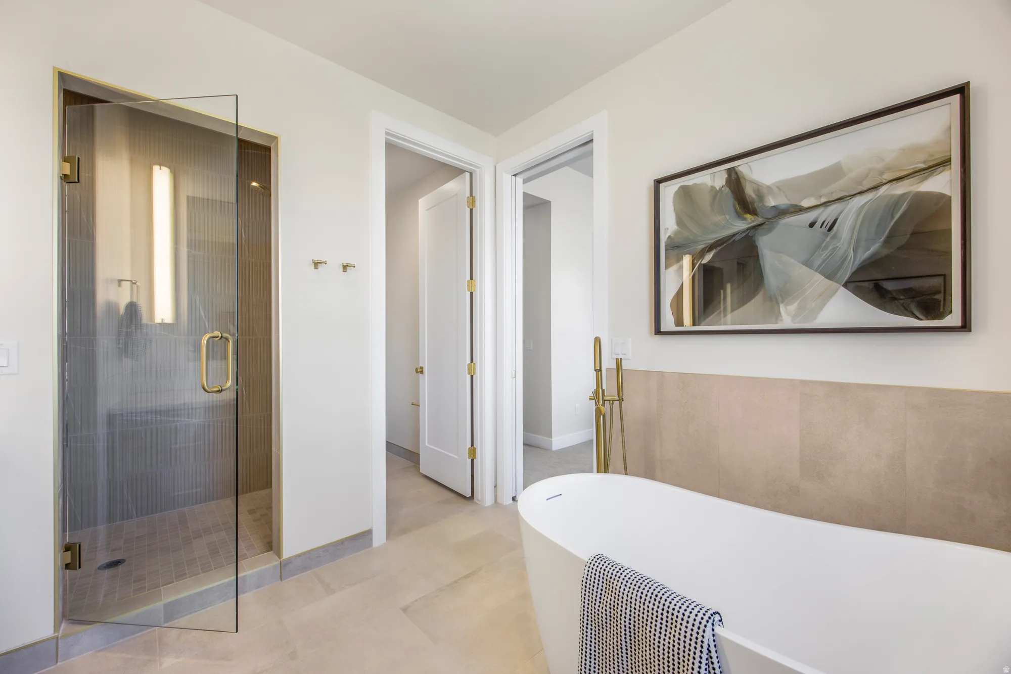 Freestanding bathtub with floor-mounted faucet, walk-in shower with glass enclosure, and large format wall tile