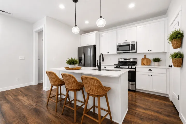 Kitchen featuring white cabinetry, stainless steel appliances, a center island with sink, pendant lighting, and wood-finish flooring