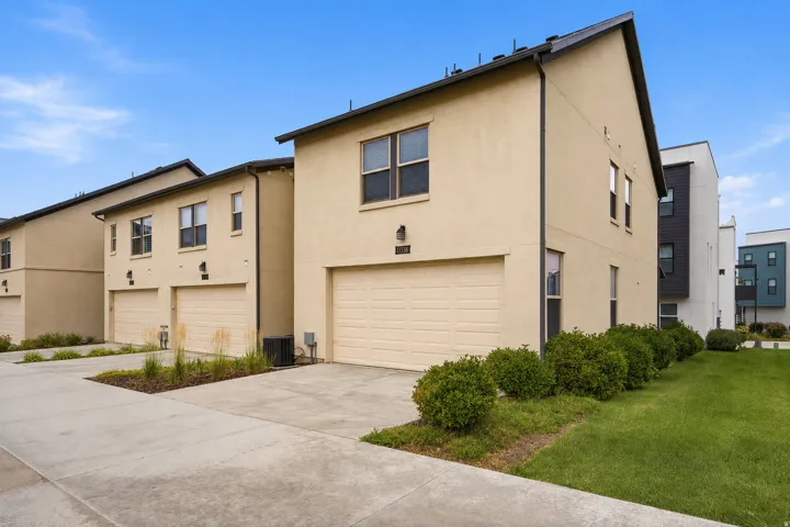 Contemporary stucco exterior, attached garage, concrete driveway, manicured lawn, and mature shrubbery